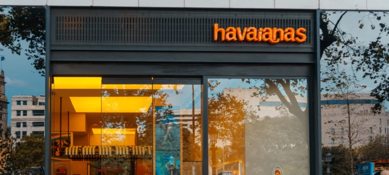 Fachada de uma loja da Havaianas, com o nome da marca escrito em laranja em um fundo preto. Abaixo, uma vitrine da loja.