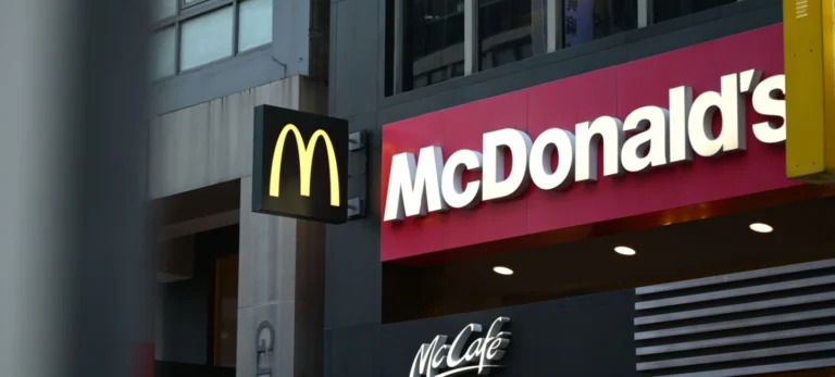 Logo do McDonald's está ao lado de um letreiro de uma loja com o nome do restaurante. Abaixo, está escrito McCafé em branco num fundo preto.