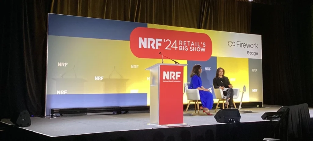 Suzy Davidkhanian, VP da Insider Intelligence, entrevista Anshu Bhardwaj, sênior VP e COO da Walmart Global Technology e Walmart Commerce Technologies no palco da NRF 2024. As duas estão sentadas em cadeiras no palco, e atrás há um painel com o nome do evento.