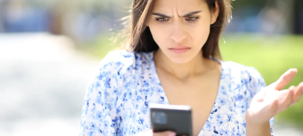 Mulher branca, olhando para celular com a expressão de desconfiança.