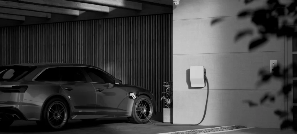 A foto em preto e branco mostra um carro elétrico abastecendo em um ponto de recarregamento elétrico.