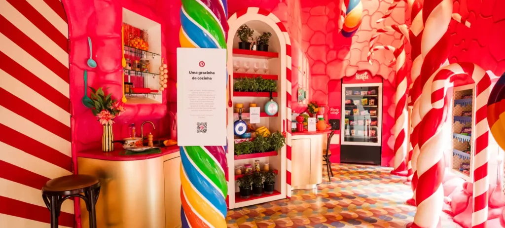 Entrada do bar secreto Secret Sweets, decorado com a tendência "Uma gracinha de cozinha", com artigos de cozinha coloridos, e uma decoração de doces, como pirulitos, balas e chocolates.