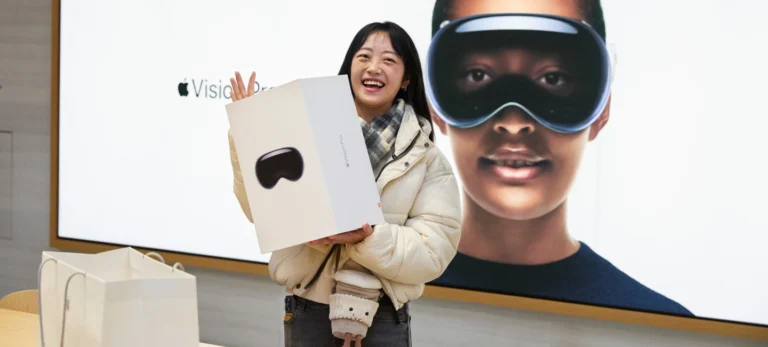 Uma cliente segura a caixa do produto Apple Vision Pro na loja da Apple, em Nova York. Atrás dela, há uma imagem de outra mulher usando o dispositivo.