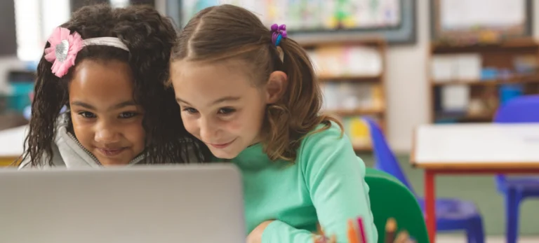 Duas meninas entre 8 e 10 anos olham para a tela de um computador.