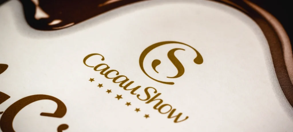 Foto mostra o logo tipo da Cacau Show escrito em marrom sobre um fundo branco.