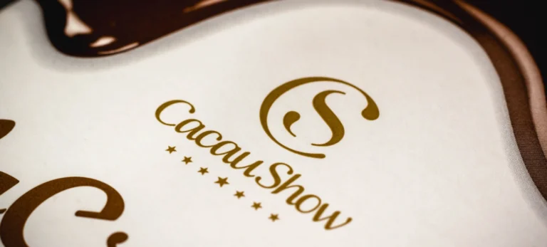 Foto mostra o logo tipo da Cacau Show escrito em marrom sobre um fundo branco.