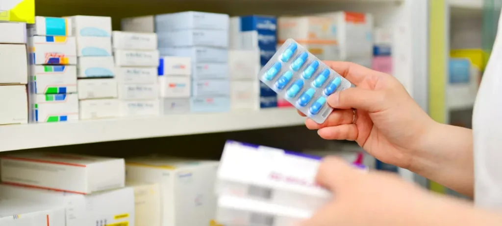 Um farmacêutico segura uma cartela de medicamentos em uma mãe, e uma caixa fechada na outra.