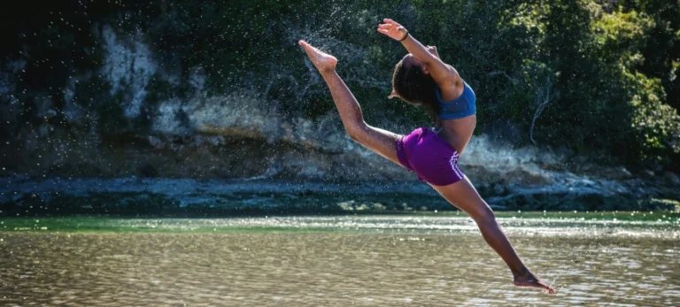 Uma mulher dança sobre uma lagoa. Atrás dela, há uma cachoeira.