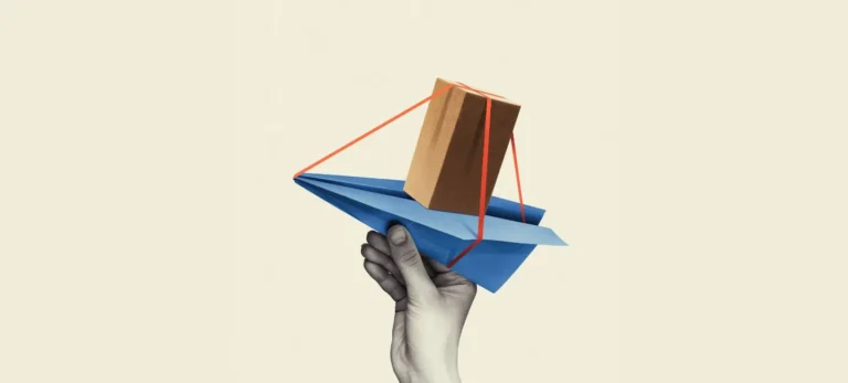 Uma mão segura um avião de papel, que carrega um pacote de papelão.
