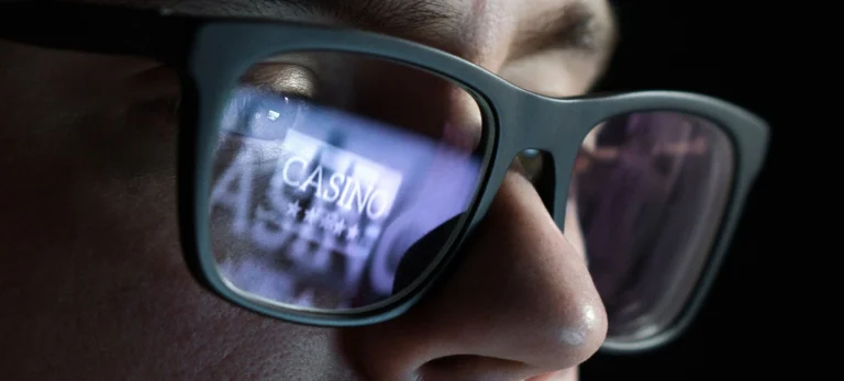 Um homem usa óculos, que reflete a tela do computador, mostrando que ele está numa aposta online.