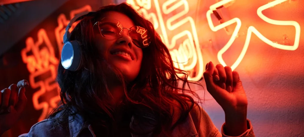 Uma mulher usa headphones. Atrás delas, luzes neon vermelhas iluminam seu rosto e seu cabelo.