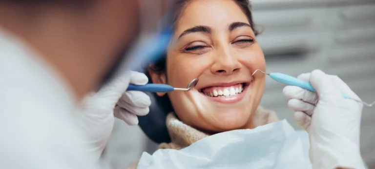Uma mulher sorri para um dentista, que segura alguns utensílios perto de seu rosto.