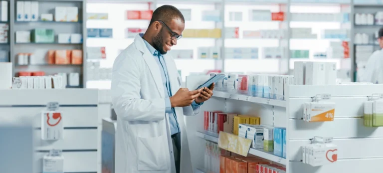 Um homem de jaleco observa produtos numa prateleira de uma farmácia.