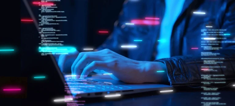 Um homem está sentado e programando em um computador, apoiado em uma mesa à sua frente.