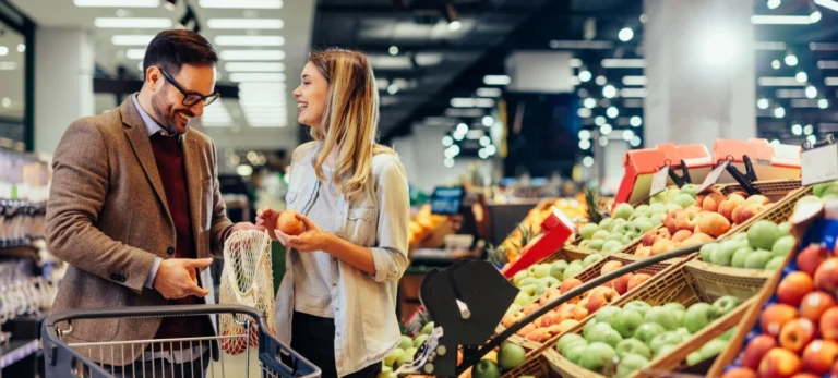 Um homem e uma mulher sorriem enquanto selecionam verduras em um supermercado.