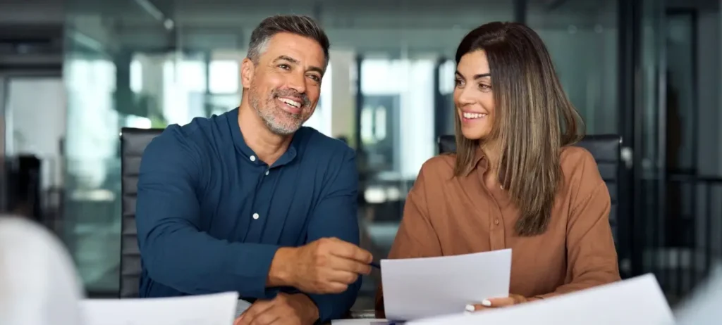 Um homem e uma mulher, que formam um casal, sorriem ao conversar com gerentes de um banco. Eles seguram folhas de papel.