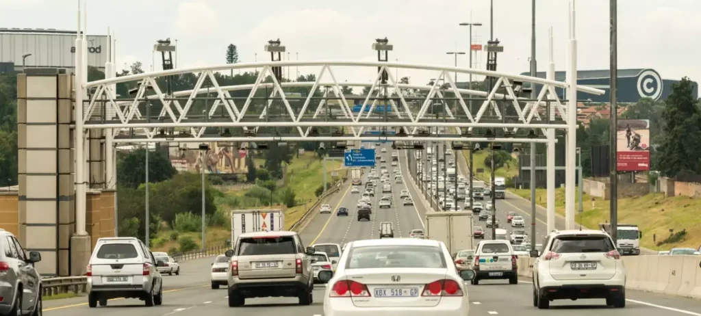 Carros, veículos e tráfego viajam em uma rodovia pedagiada sob pórticos de pedágio elevados que atravessam a autoestrada na África do Sul.