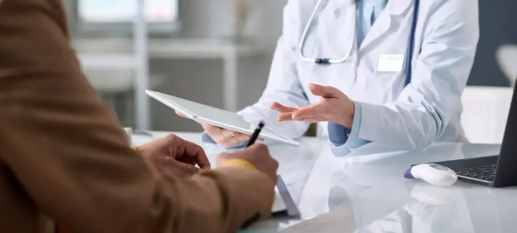 Uma médica atende um paciente, e segura uma prancheta.