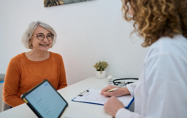 Profissional de saúde conversa com uma paciente idosa durante consulta em consultório médico.